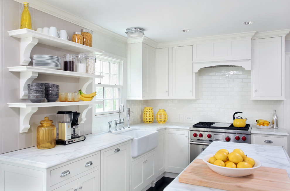 This is an example of a traditional l-shaped kitchen in Chicago with a farmhouse sink, shaker cabinets, white cabinets, white splashback, subway tile splashback, stainless steel appliances and with island.