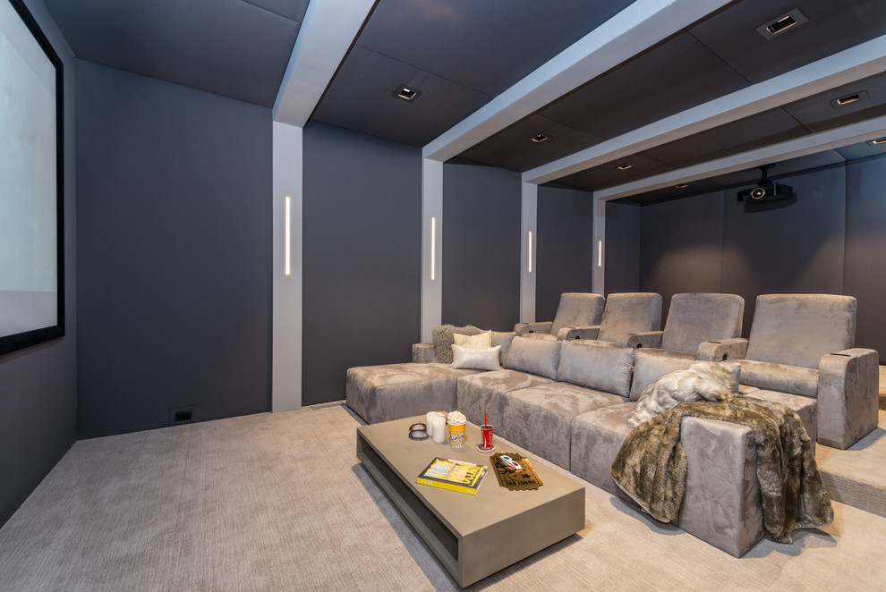 This is an example of an expansive contemporary enclosed home theatre in New York with grey walls, beige floor, carpet and a projector screen.