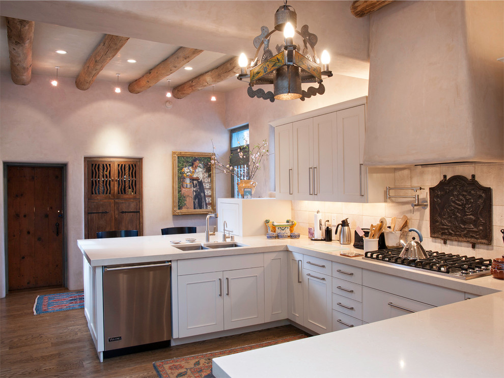 This is an example of a mediterranean u-shaped kitchen in Albuquerque with an undermount sink, white cabinets, white splashback, solid surface benchtops, stone tile splashback, stainless steel appliances and medium hardwood floors.