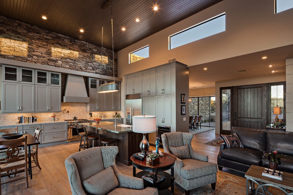 Open concept kitchen - mid-sized rustic l-shaped light wood floor open concept kitchen idea in Phoenix with a drop-in sink, raised-panel cabinets, gray cabinets, granite countertops, beige backsplash, stone tile backsplash, stainless steel appliances and an island