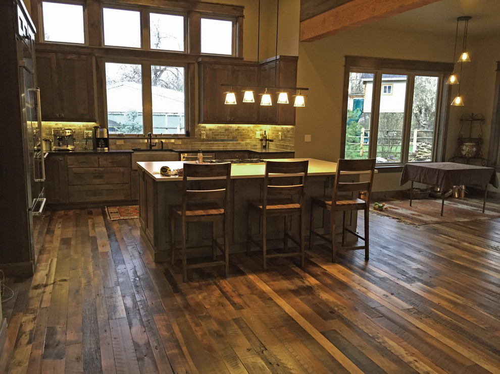 Inspiration for a large country l-shaped kitchen in Boise with a farmhouse sink, shaker cabinets, dark wood cabinets, grey splashback, subway tile splashback, stainless steel appliances, medium hardwood floors, with island and brown floor.
