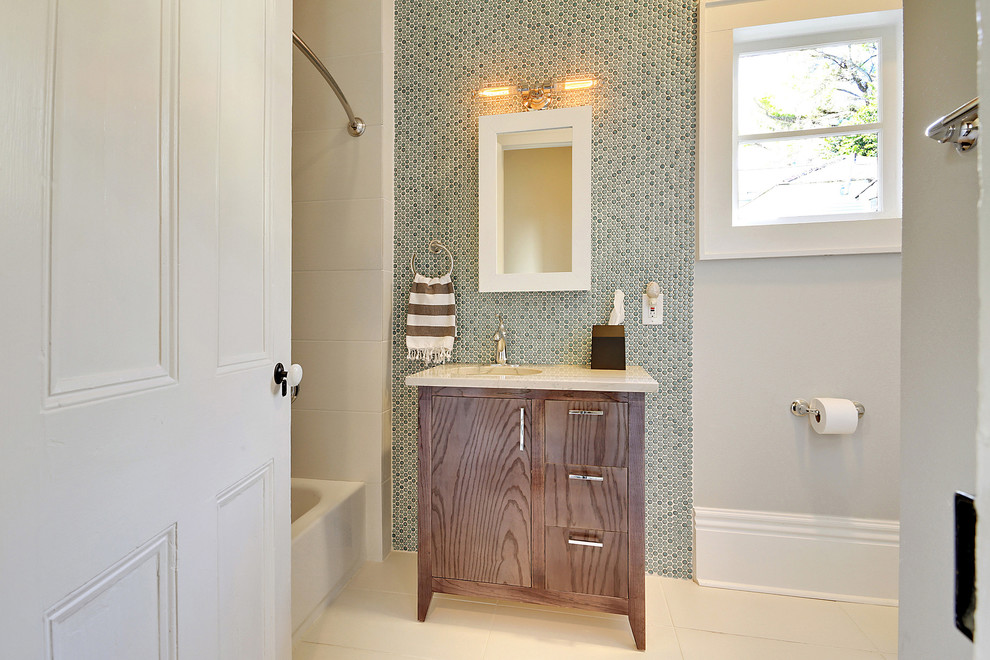 This is an example of a mid-sized transitional 3/4 bathroom in New Orleans with dark wood cabinets, an alcove tub, a shower/bathtub combo, blue tile, mosaic tile, flat-panel cabinets, grey walls, an integrated sink, engineered quartz benchtops, beige floor, a shower curtain and white benchtops.