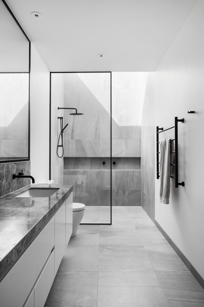 Design ideas for a large modern master bathroom in Melbourne with an open shower, a two-piece toilet, gray tile, porcelain tile, white walls, porcelain floors, an undermount sink, marble benchtops, grey floor, grey benchtops, a niche, a single vanity and a built-in vanity.