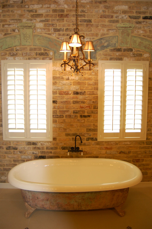 Photo of a large master bathroom in Austin with a claw-foot tub and brick walls.