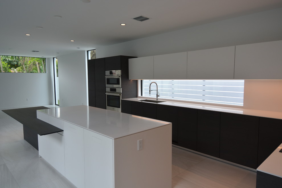 Expansive modern l-shaped eat-in kitchen in Miami with an undermount sink, flat-panel cabinets, white cabinets, solid surface benchtops, window splashback, stainless steel appliances, ceramic floors and with island.