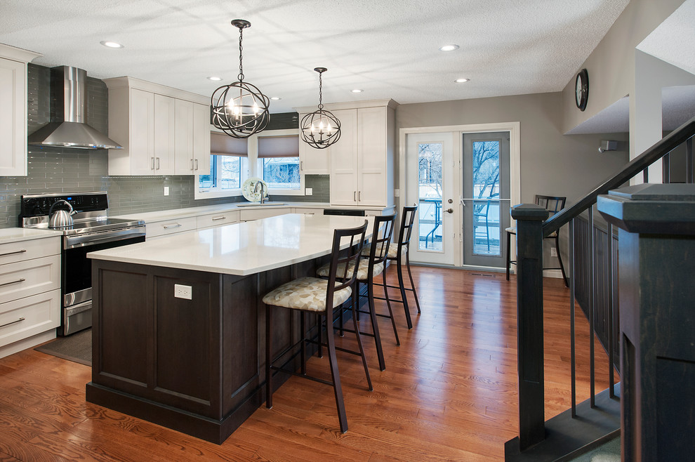 Example of a large transitional l-shaped dark wood floor eat-in kitchen design in Calgary with an undermount sink, recessed-panel cabinets, white cabinets, solid surface countertops, green backsplash, glass tile backsplash, stainless steel appliances and an island