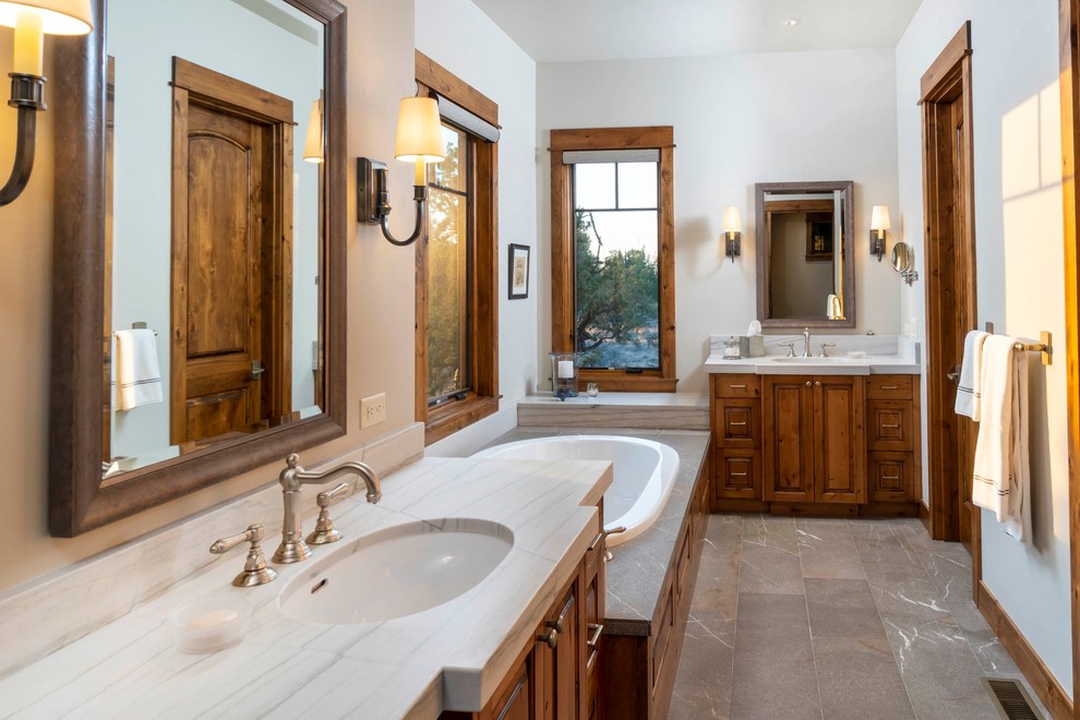 Inspiration for a mid-sized rustic master brown floor drop-in bathtub remodel with beige walls, an undermount sink, raised-panel cabinets, medium tone wood cabinets, marble countertops and white countertops