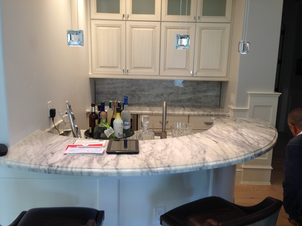 Inspiration for a large arts and crafts l-shaped seated home bar in Phoenix with a drop-in sink, raised-panel cabinets, white cabinets, marble benchtops, grey splashback, marble splashback, painted wood floors, brown floor and grey benchtop.