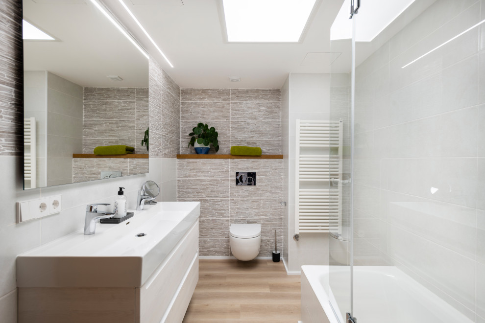 Mid-sized modern master bathroom in Palma de Mallorca with white cabinets, a drop-in tub, a one-piece toilet, gray tile, grey walls, medium hardwood floors, beige floor, an enclosed toilet, a double vanity and a floating vanity.
