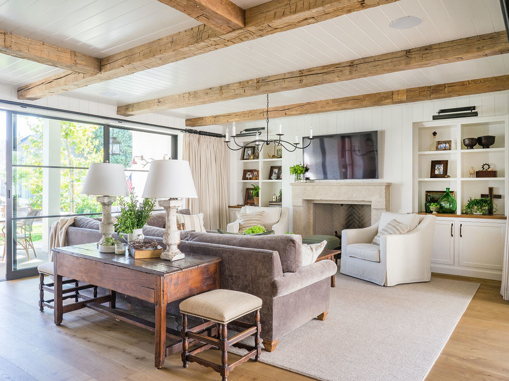 This is an example of a beach style family room in Orange County with white walls, light hardwood floors, a standard fireplace and a wall-mounted tv.