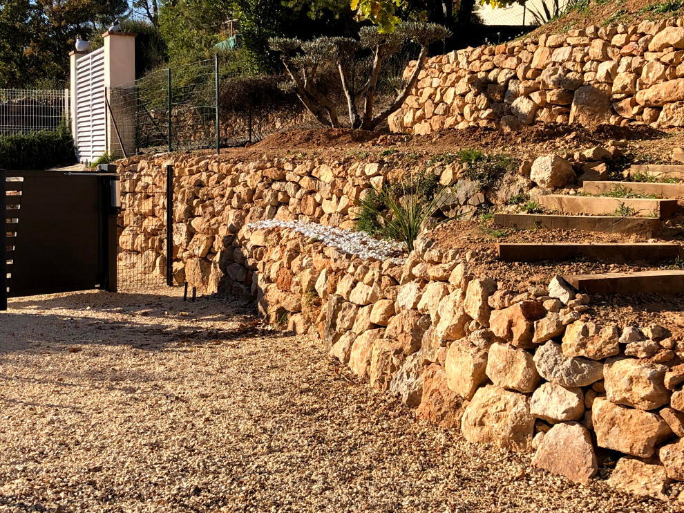 This is an example of a large traditional sloped garden in Nice with a retaining wall and a stone fence.