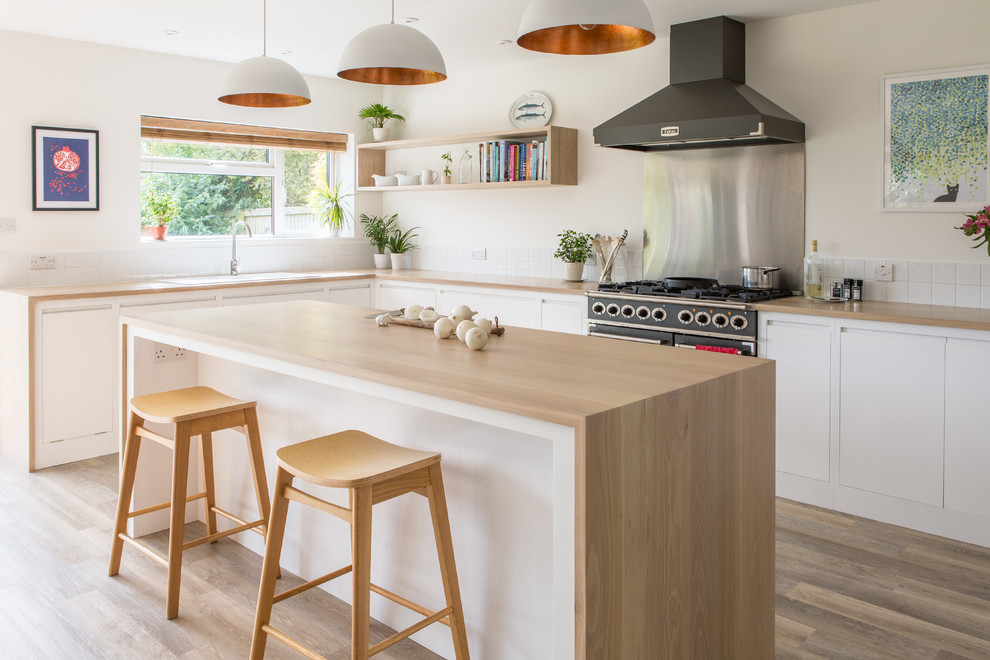 Photo of a large contemporary u-shaped open plan kitchen in Other with a double-bowl sink, flat-panel cabinets, white cabinets, wood benchtops, white splashback, porcelain splashback, light hardwood floors and with island.