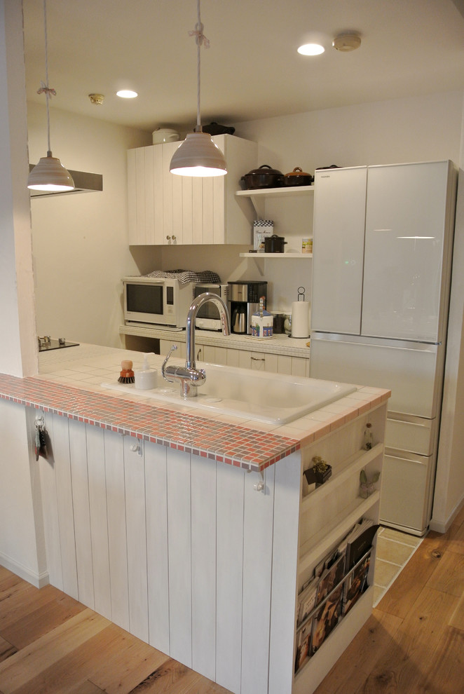 Photo of a small country galley open plan kitchen in Nagoya with a drop-in sink, flat-panel cabinets, white cabinets, tile benchtops, white splashback, subway tile splashback, white appliances, no island and ceramic floors.