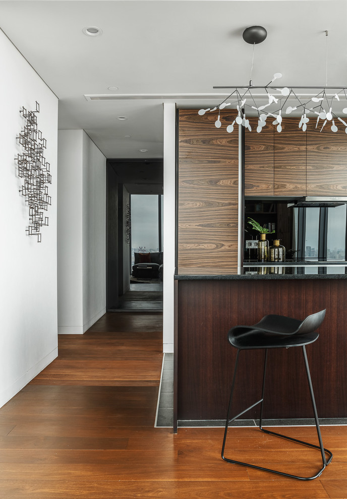 Design ideas for a mid-sized contemporary single-wall open plan kitchen in Moscow with an undermount sink, flat-panel cabinets, medium wood cabinets, quartz benchtops, black splashback, glass sheet splashback, porcelain floors, with island, black floor and black appliances.