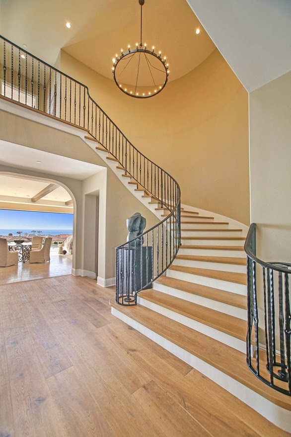 Photo of a large mediterranean wood curved staircase in Orange County with wood risers and metal railing.