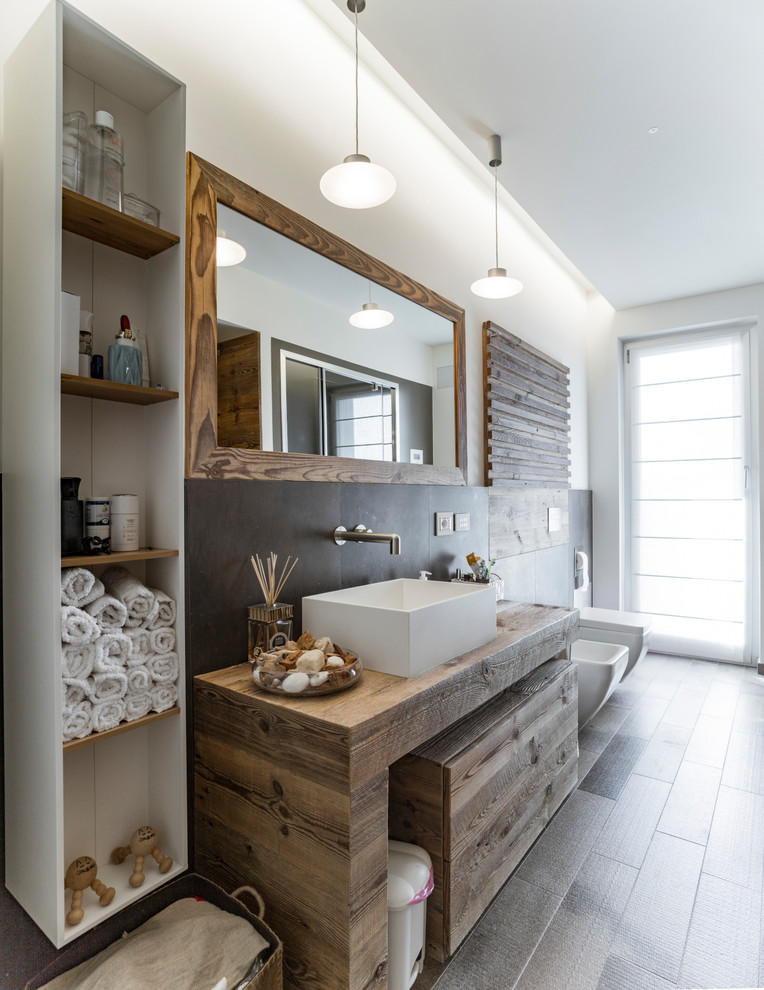 Inspiration for a beach style 3/4 bathroom in Turin with dark wood cabinets, gray tile, a vessel sink, wood benchtops, a bidet, white walls and brown benchtops.