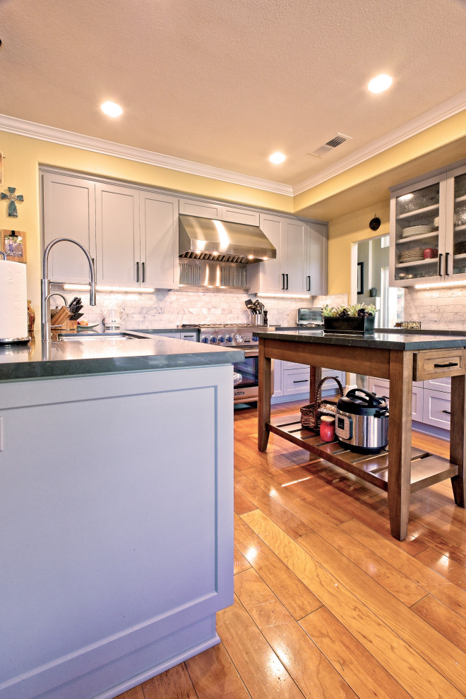 This is an example of a large transitional kitchen in Los Angeles with an undermount sink, shaker cabinets, grey cabinets, quartz benchtops, grey splashback, ceramic splashback, stainless steel appliances, medium hardwood floors, with island, brown floor, black benchtop and recessed.