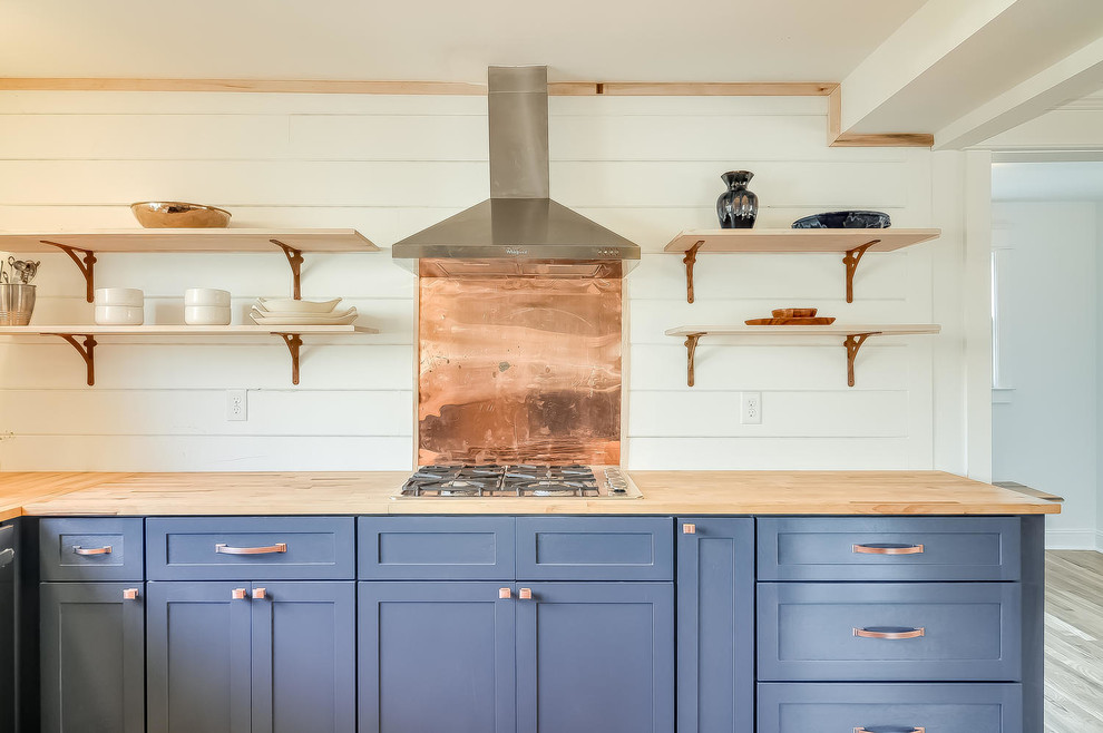 Design ideas for a mid-sized traditional u-shaped eat-in kitchen in Nashville with a farmhouse sink, shaker cabinets, blue cabinets, wood benchtops, white splashback, stainless steel appliances and light hardwood floors.