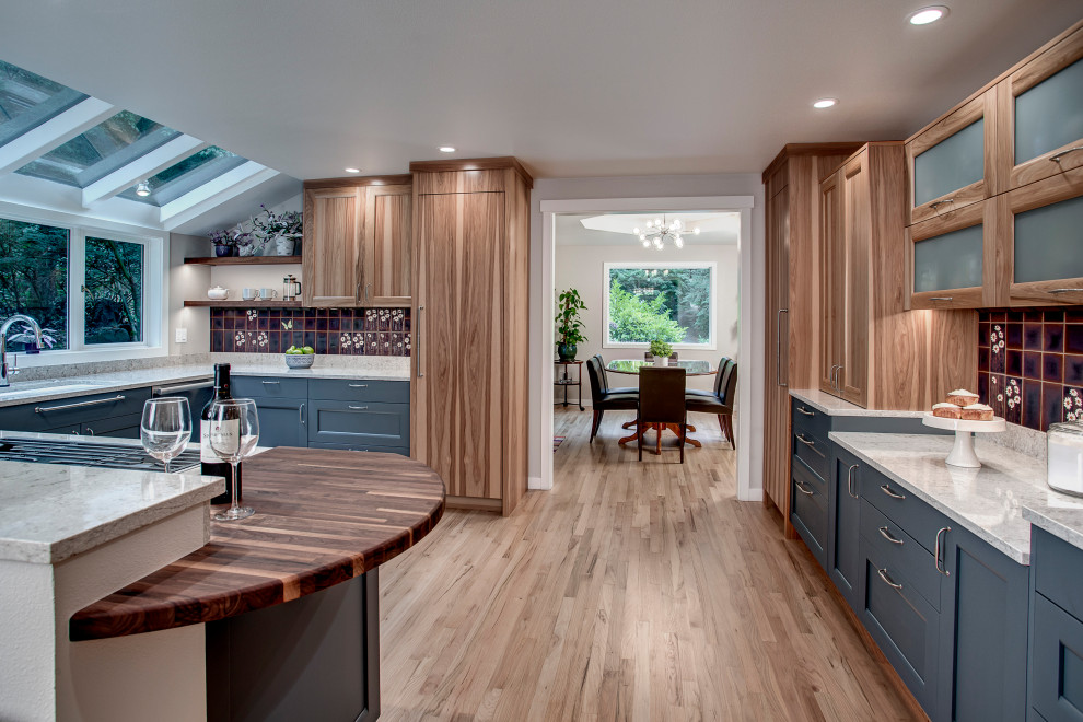 Inspiration for a large eclectic u-shaped open plan kitchen in Seattle with a farmhouse sink, flat-panel cabinets, blue cabinets, quartz benchtops, multi-coloured splashback, ceramic splashback, stainless steel appliances, light hardwood floors, a peninsula, brown floor and grey benchtop.