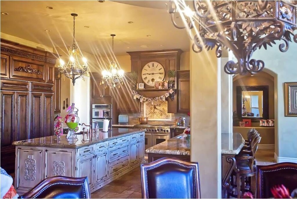 Large transitional l-shaped travertine floor and brown floor eat-in kitchen photo in Phoenix with a farmhouse sink, raised-panel cabinets, medium tone wood cabinets, granite countertops, brown backsplash, stainless steel appliances and an island