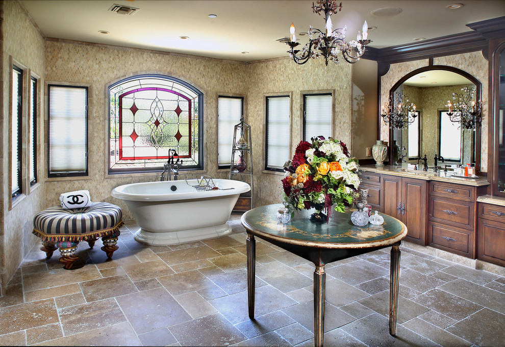This is an example of an expansive mediterranean master bathroom in Los Angeles with an undermount sink, furniture-like cabinets, dark wood cabinets, granite benchtops, a freestanding tub, beige tile, mosaic tile, beige walls and travertine floors.