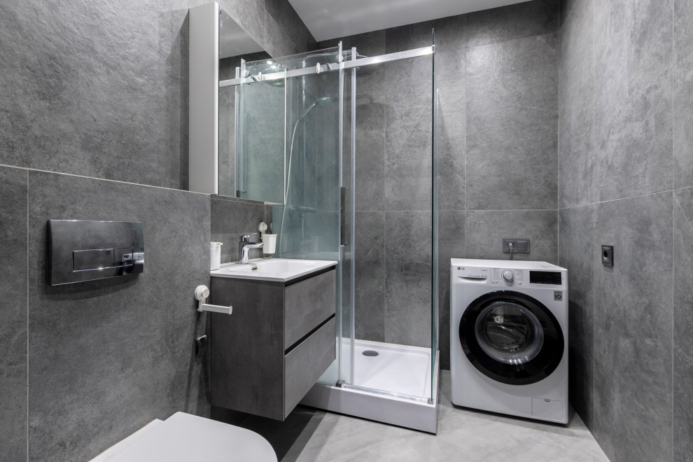 Exempel på ett mellanstort industriellt badrum med dusch, med släta luckor, grå skåp, en kantlös dusch, en vägghängd toalettstol, grå kakel, porslinskakel, grå väggar, klinkergolv i porslin, ett integrerad handfat, grått golv och dusch med skjutdörr