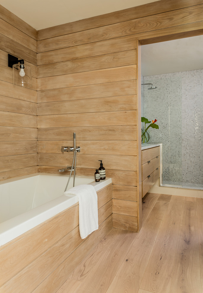 This is an example of a contemporary master bathroom in Boston with light wood cabinets, beige walls, light hardwood floors, beige floor, flat-panel cabinets, a drop-in tub, blue tile, mosaic tile, a single vanity, a floating vanity, wood walls, a corner shower, an open shower and grey benchtops.