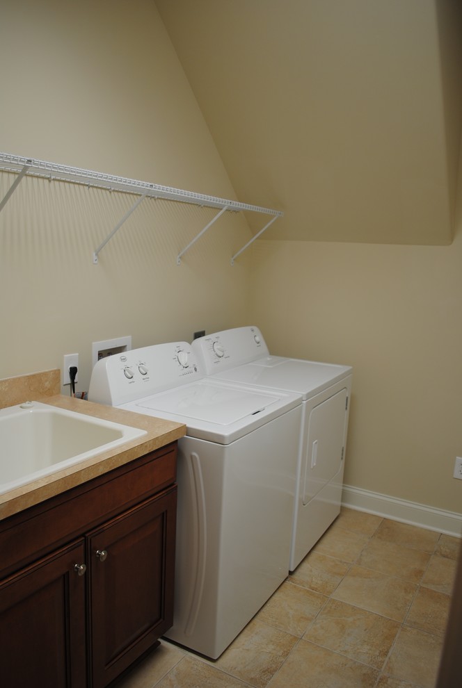 Photo of a mid-sized traditional single-wall dedicated laundry room in Other with a drop-in sink, raised-panel cabinets, dark wood cabinets, laminate benchtops, beige walls, travertine floors, a side-by-side washer and dryer, brown floor and brown benchtop.