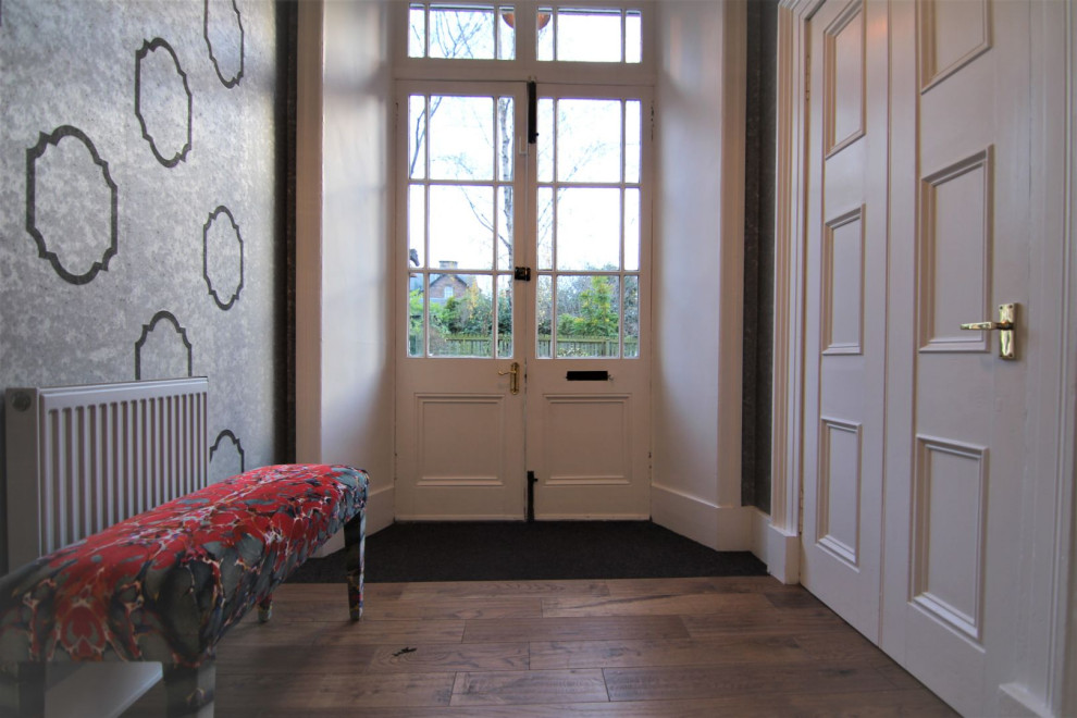 Modelo de entrada minimalista con paredes metalizadas, suelo de madera oscura, puerta doble, puerta blanca y papel pintado