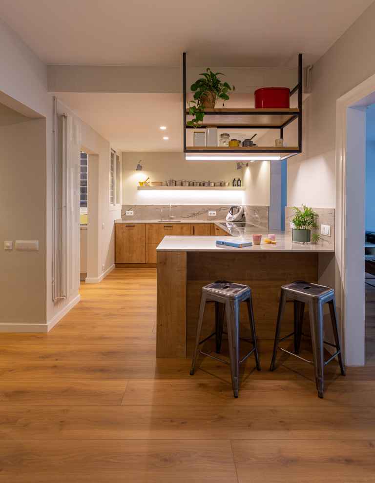 This is an example of a large contemporary u-shaped open plan kitchen in Barcelona with a single-bowl sink, medium wood cabinets, limestone benchtops, beige splashback, limestone splashback, stainless steel appliances, medium hardwood floors, a peninsula, brown floor, beige benchtop and recessed.