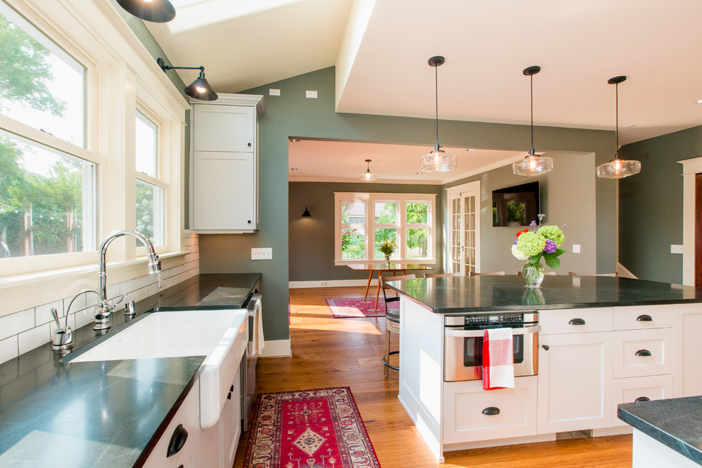 Photo of a large traditional u-shaped open plan kitchen in Seattle with a farmhouse sink, shaker cabinets, white cabinets, soapstone benchtops, white splashback, subway tile splashback, stainless steel appliances, medium hardwood floors, with island and multi-coloured benchtop.