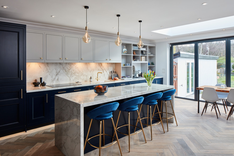 Design ideas for a large contemporary galley open plan kitchen in London with a drop-in sink, shaker cabinets, blue cabinets, marble benchtops, white splashback, marble splashback, panelled appliances, light hardwood floors, with island, brown floor and white benchtop.