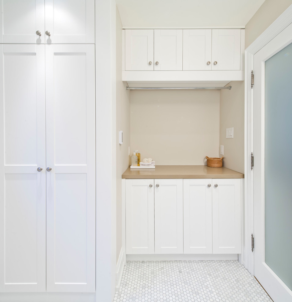 Small contemporary single-wall laundry room in Toronto with shaker cabinets, white cabinets, beige walls, marble floors and a stacked washer and dryer.
