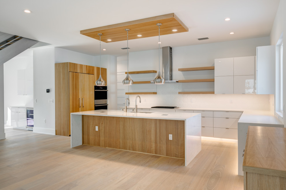 Large minimalist u-shaped light wood floor and beige floor open concept kitchen photo in Tampa with a single-bowl sink, flat-panel cabinets, white cabinets, quartz countertops, white backsplash, ceramic backsplash, stainless steel appliances, an island and white countertops