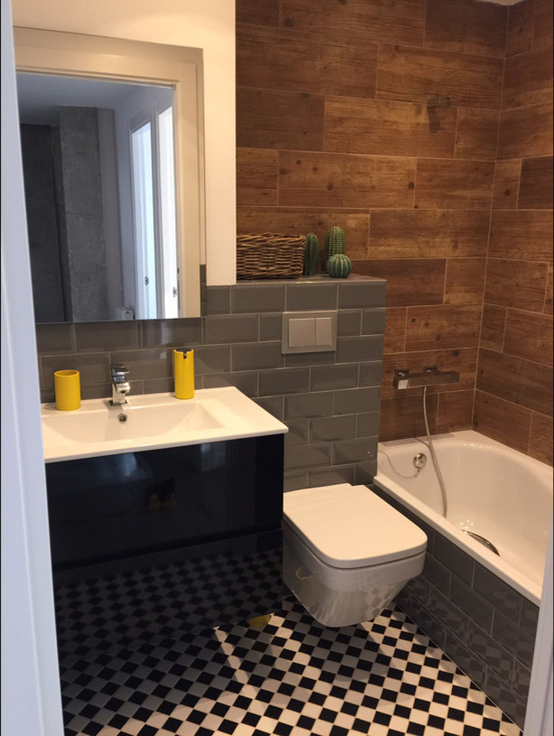 This is an example of a small industrial kids bathroom in Other with furniture-like cabinets, black cabinets, a drop-in tub, a wall-mount toilet, gray tile, mosaic tile, brown walls, ceramic floors, an integrated sink and white floor.