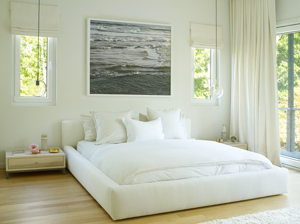 Photo of a mid-sized beach style master bedroom in New York with white walls, light hardwood floors and beige floor.