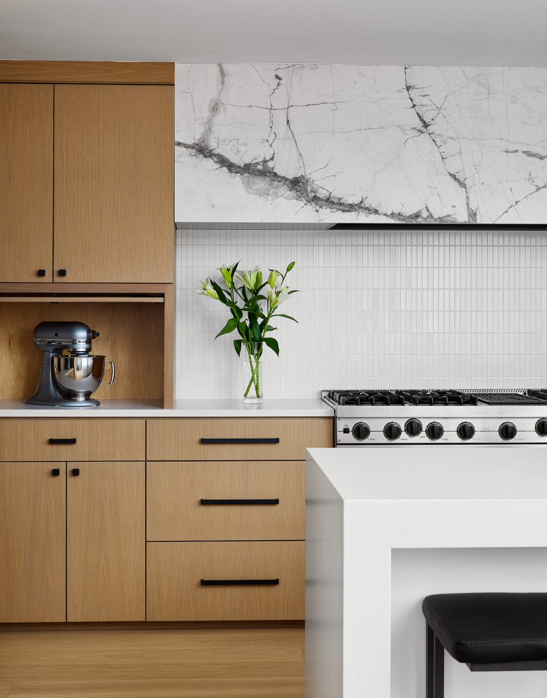 This is an example of a modern u-shaped open plan kitchen in Chicago with flat-panel cabinets, white splashback, mosaic tile splashback, stainless steel appliances, a peninsula and white benchtop.