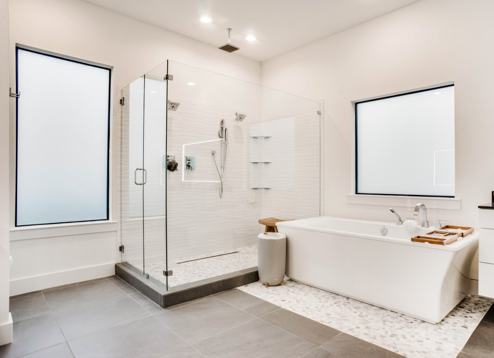 Design ideas for a contemporary master bathroom in Dallas with flat-panel cabinets, white cabinets, a freestanding tub, white tile, white walls, grey floor and a hinged shower door.