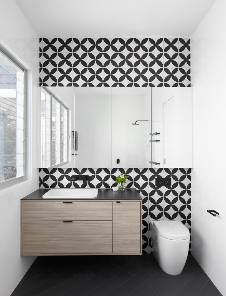 Inspiration for a mid-sized contemporary master bathroom in Melbourne with light wood cabinets, a wall-mount toilet, multi-coloured walls, a drop-in sink, a freestanding tub, an open shower, multi-coloured tile, mosaic tile, solid surface benchtops, black benchtops and flat-panel cabinets.