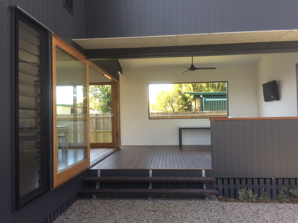 This is an example of a small contemporary backyard and ground level deck in Brisbane with a roof extension and wood railing.