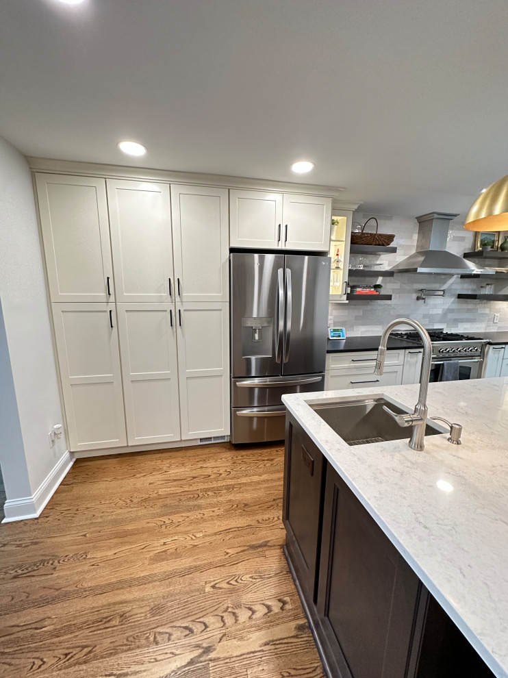 Inspiration for a large transitional l-shaped eat-in kitchen in Philadelphia with an undermount sink, recessed-panel cabinets, white cabinets, quartz benchtops, grey splashback, porcelain splashback, stainless steel appliances, light hardwood floors, with island, brown floor and white benchtop.