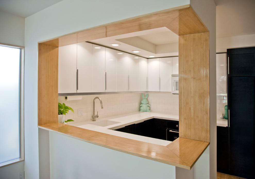 Design ideas for a modern u-shaped kitchen in San Diego with flat-panel cabinets, white cabinets, white splashback, subway tile splashback and black appliances.