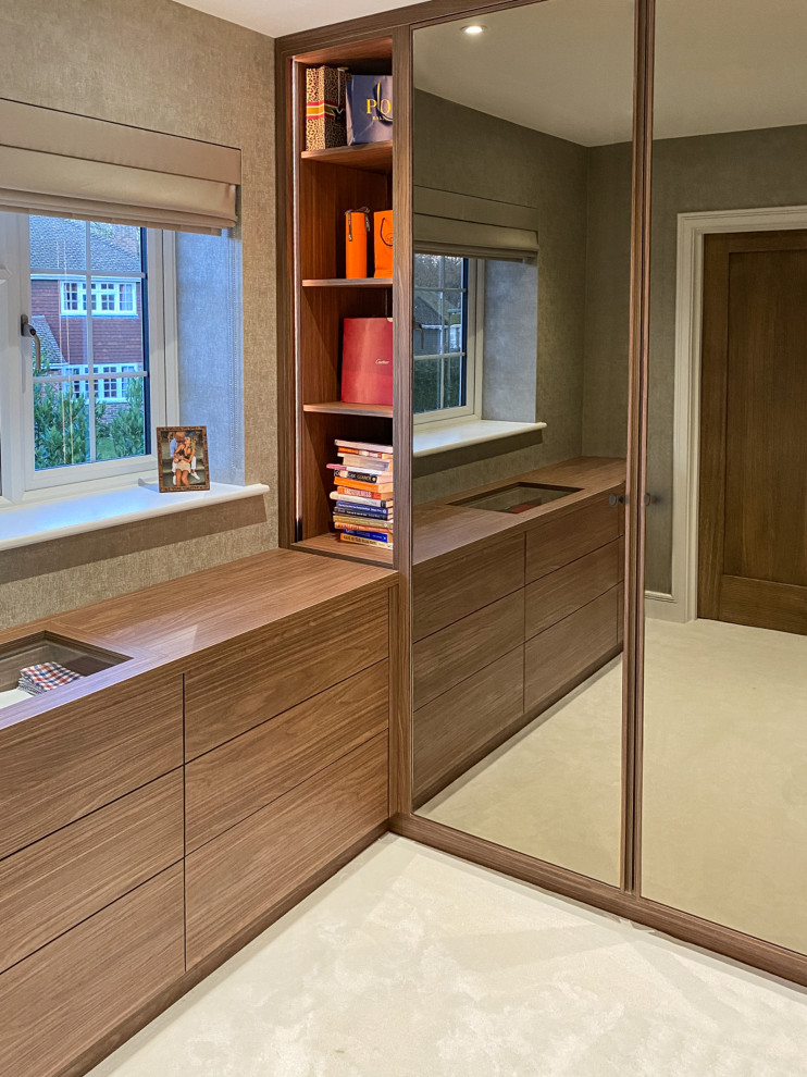 Design ideas for a medium sized modern built-in wardrobe in Buckinghamshire with carpet, beige floors, glass-front cabinets and medium wood cabinets.