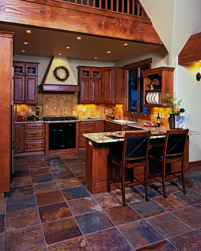 Design ideas for a mid-sized transitional u-shaped eat-in kitchen in Denver with an undermount sink, raised-panel cabinets, medium wood cabinets, granite benchtops, beige splashback, stone tile splashback, black appliances, slate floors, with island, brown floor and brown benchtop.