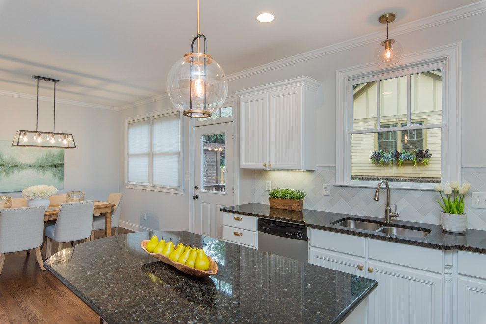 This is an example of a transitional l-shaped eat-in kitchen in Atlanta with an undermount sink, beaded inset cabinets, white cabinets, granite benchtops, white splashback, marble splashback, stainless steel appliances, medium hardwood floors, with island, brown floor and black benchtop.