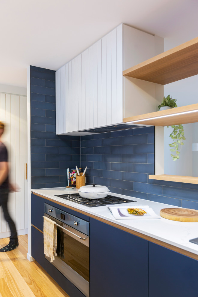 This is an example of a medium sized modern galley kitchen pantry in Canberra - Queanbeyan with a built-in sink, blue cabinets, engineered stone countertops, blue splashback, cement tile splashback, stainless steel appliances, medium hardwood flooring and white worktops.