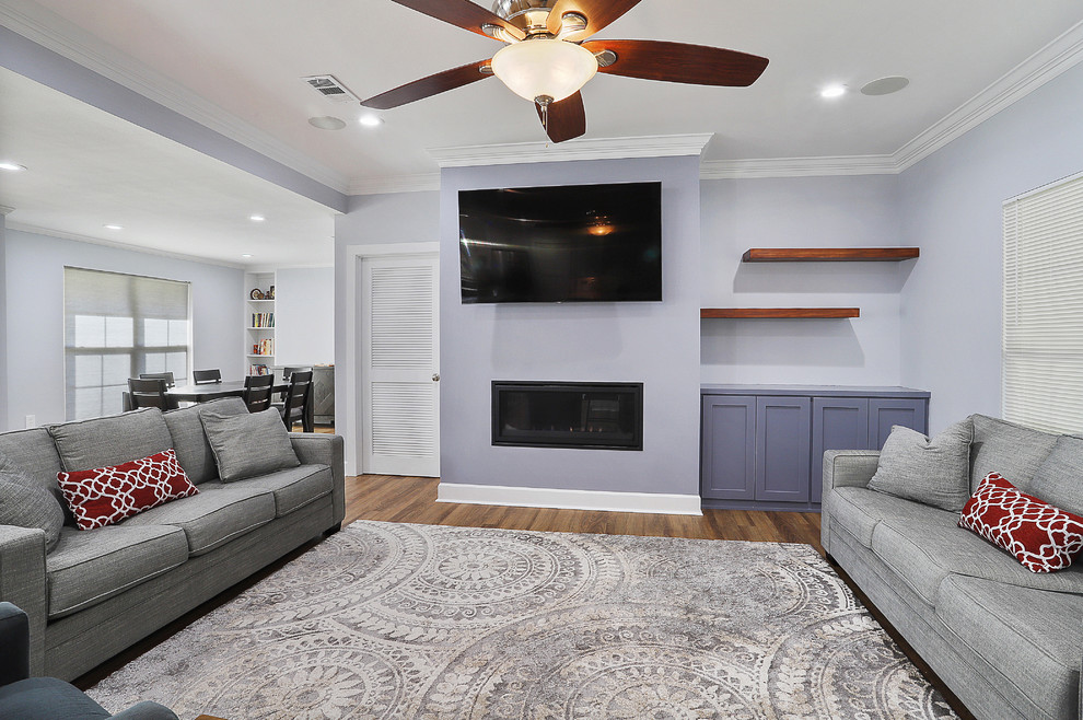 This is an example of a mid-sized transitional open concept family room in New Orleans with vinyl floors, a standard fireplace, a wall-mounted tv, brown floor, grey walls and a plaster fireplace surround.