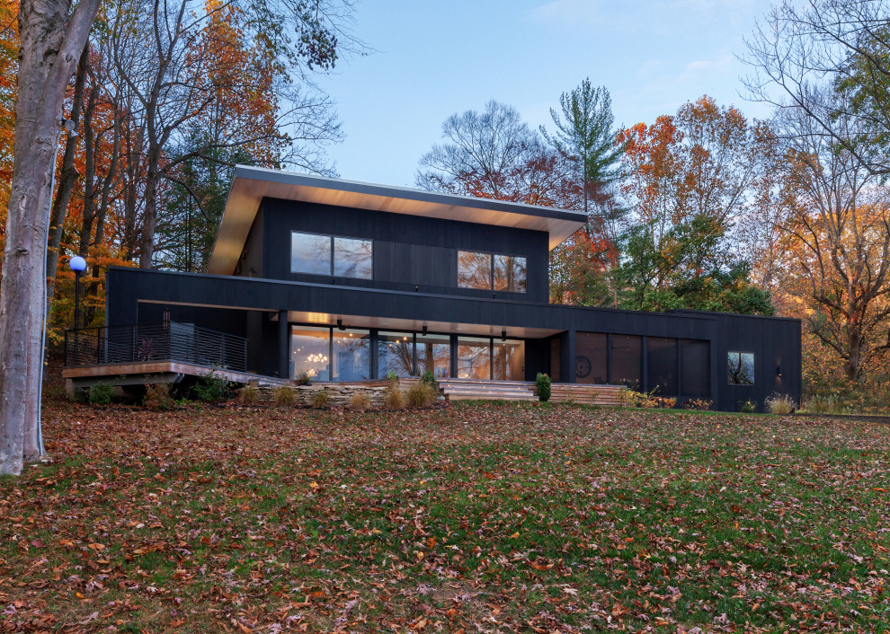 Esempio della facciata di una casa nera moderna a due piani di medie dimensioni con rivestimento in legno, copertura in metallo o lamiera, tetto grigio, pannelli sovrapposti e terreno in pendenza