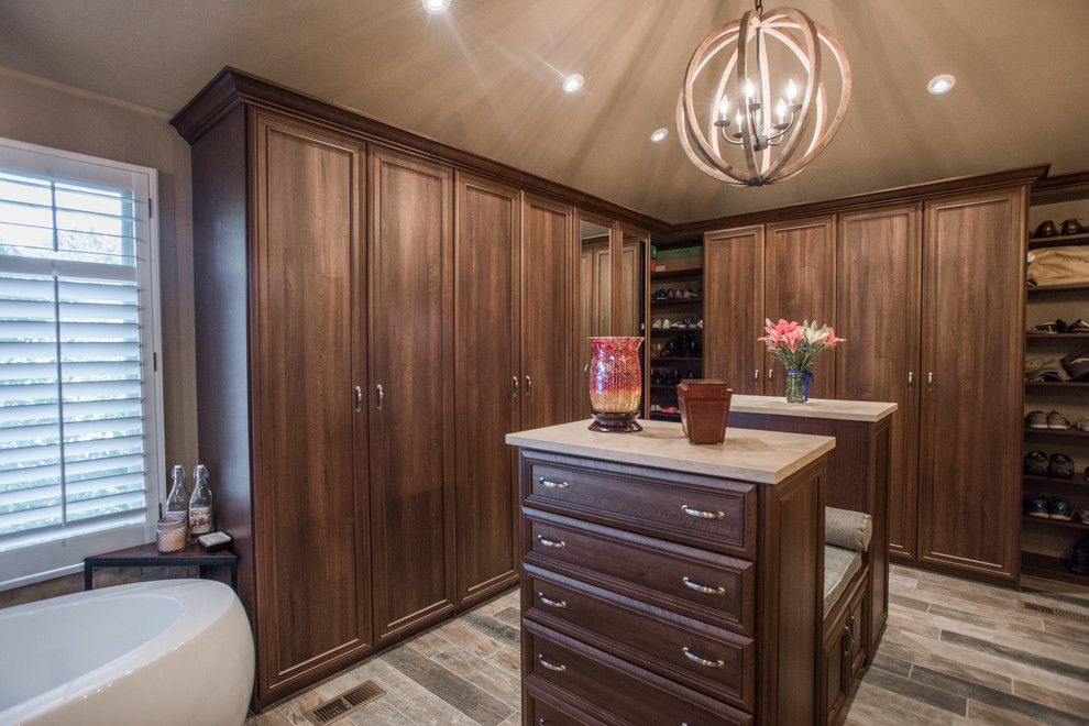 Large traditional gender-neutral walk-in wardrobe in Denver with raised-panel cabinets, medium wood cabinets, plywood floors and brown floor.