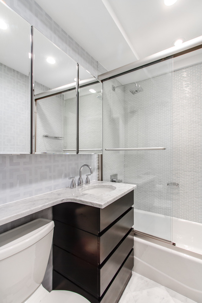 Small modern master bathroom in New York with an undermount sink, flat-panel cabinets, dark wood cabinets, marble benchtops, an alcove tub, a shower/bathtub combo, a two-piece toilet, gray tile, glass tile, grey walls and marble floors.